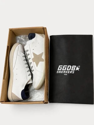Golden Goose vita sneakers med stjärna💎 - Säljer ett par sjukt snygga Golden Goose Superstar sneakers i nyskick 🤍 Endast testade, annars helt nya och kommer med box, dustbag samt Golden Goose-pass 👟✨  • Modell: Superstar • Färg: Vit/beige med mörkblå detalj • Skick: Helt nya • Allt på bilderna ingår • Väldigt clean och lättmatchad modell  Perfekta till både vardag och finare outfits 🔥 Pris: 2 299 kr — först till kvarn!