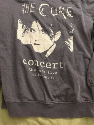 The Cure tjocktröja - Grå sweatshirt med tryck av The Cure, har en liten vit fläck på en av ärmarna men bortsett från det är den i bra skick. Storlek xs men passar mer som S-M!!