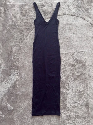Svart långklänning från H&M - En svart långklänning från H&M med djup v-ringning och smala axelband. Klänningen har en figurnära passform och är tillverkad i ett stretchigt material som känns bekvämt mot kroppen. Perfekt för dig som gillar en stilren och enkel look.