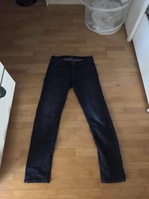 Mörkblå slim fit jeans från Lee W32 L34 - Säljer ett par mörkblå slim fit jeans från Lee med klassisk femficksdesign och Lee-lapp bak i midjan. Jeansen har smal passform och är tillverkade i stretchigt denimtyg för extra komfort. Perfekta till en avslappnad stil.