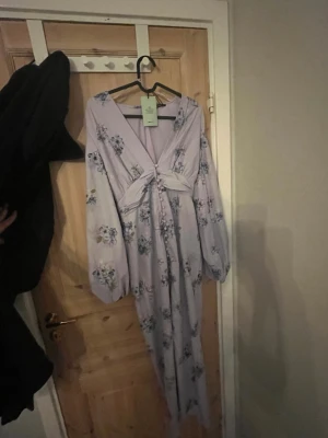 Ballon sleeve dress från gina tricot  - Supersöt långklänning i ljuslila från Gina Tricot med blommigt mönster och ballongärmar. Klänningen har v-ringning och markerad midja, perfekt för vår och sommar. Materialet är mjukt och lätt, vilket gör den bekväm att bära hela dagen.