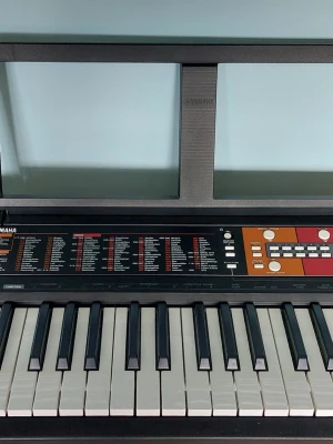 Yamaha keyboard med notställ - Elektroniskt keyboard från Yamaha med svart och vit design, inbyggda knappar och reglage för olika ljud och rytmer. Tangenter i plast och medföljande notställ. Perfekt för dig som vill spela musik hemma eller öva på nya låtar.
