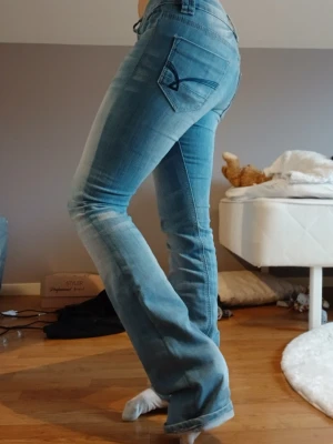 Lågmidjade bootcut jeans från Riever - Snygga ljusblå bootcut jeans från Riever med slitningar och tvättade detaljer. Storleken står ej men passar mig som använder 34. Jag är 152 cm lång men som ni ser på bilden så är dem alldeles för långa. Dem går ej att köpa längre någonstans och är därför vintage. Jeansen har dubbla knappar i midjan, klassiska fickor och en broderad detalj på bakfickan.