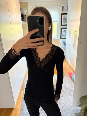 Spetströja  - Svart långärmad topp med djup v-ringning och fina spetsdetaljer längs halsringningen och ärmsluten. 