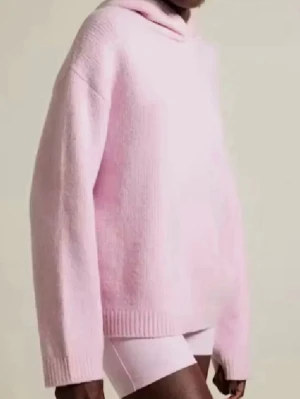 Ljusrosa stickad hoodie - Mysig ljusrosa stickad hoodie med avslappnad passform och långa ärmar. Tröjan har ribbade muddar och en mjuk huva, perfekt för en chill och trendig look. Passar perfekt till jeans eller tights.