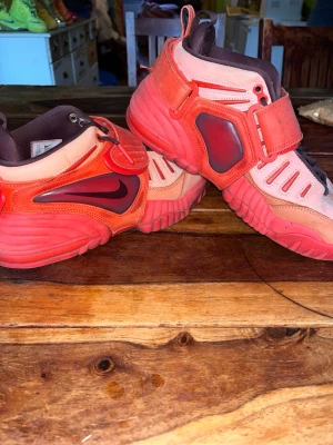 Nike x Ambush röda sneakers - Unika sneakers från Nike och Ambush i rött och orange med avtagbara detaljer och svart swoosh på sidan. Skorna har en chunky sula, coola paneler och kardborreband. Materialet är en mix av läder och syntet. Perfekta för dig som vill sticka ut med din stil.