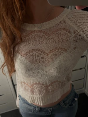 Vit transparent stickad tröja - Säljer en vit, transparent stickad tröja med vågigt spetsmönster. Tröjan har långa ärmar, rund halsringning och ribbade muddar. Perfekt för lager på lager och ger en trendig look till jeans eller kjol.