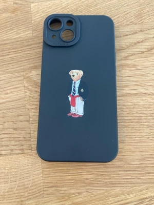 iPhone 14 Mobilskal Nyskick - Snyggt svart/mörkblått mobilskal med en stilren björn i kavaj, slips och röda byxor på baksidan. Skalet är gjort i mjukt silikonmaterial och har öppningar för kamera och knappar. Passar perfekt för dig som vill ha ett unikt och lekfullt skal till din mobil. Använd i en vecka.