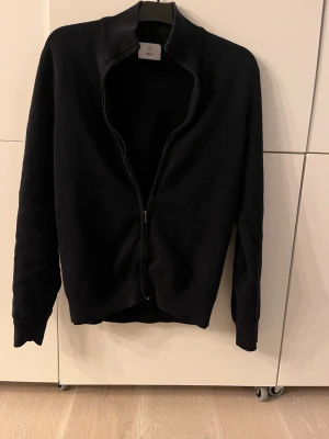 Mörkblå  ziptröja från Bläck - Klassisk mörkblå ziptröja från bläck med hög krage och hel dragkedja framtill. Tröjan har lång ärm och ribbade muddar vid ärmslut och nederkant. Perfekt att slänga på sig över en t-shirt för en clean look. 