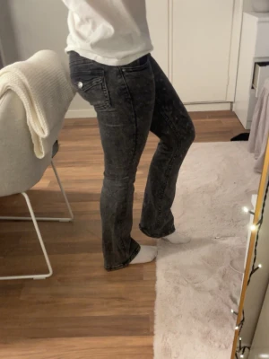 Gråa bootcut jeans med tvättad look - Säljer ett par gråa bootcut jeans med tvättad, lite sliten look. Jeansen har klassiska fem fickor och vita knappar bak. Snygg passform som sitter tajt över låren och släpper ut vid vaden. Perfekta till sneakers eller boots!