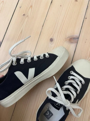 Svarta Veja sneakers med vit sula - Snygga svarta Veja sneakers med vit sula. Säljer då dom är lite små för mig, väldigt sparsamt använda och har därför inte format sig efter min fot! Super coola nu till våren! Originalpris 1500kr, men lägg gärna ett eget bud också! 