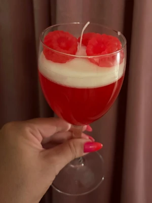 Dekorativ ljus i glas med hallon - Unikt handgjort dekorljus i ett vinglas, med röd och vit vax och två hallonformade dekorationer på toppen. Ljusen är gjorda för att likna en dessertdrink och passar perfekt som inredningsdetalj. Glaset är genomskinligt och ljuset har en tydlig veke i mitten.