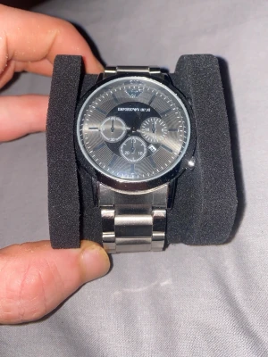 Emporio Armani silverfärgad klocka - Stilren klocka från Emporio Armani i rostfritt stål med silverfärgad länkarmband och svart urtavla. Klockan har tre subdials, datumvisning och klassisk logga vid tolvslaget. Perfekt accessoar för dig som gillar en elegant och modern look.