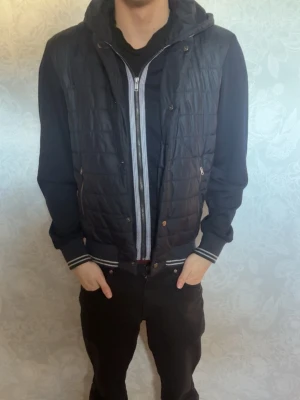 Svart cardiganjacka med huva från Zara  - Snygg svart cardiganjacka med mönster och huva. Jackan har dragkedja och tryckknappar.