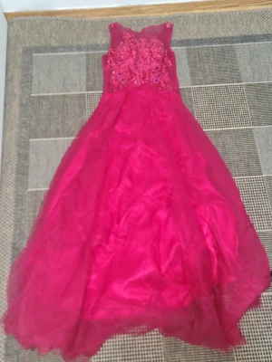 Lång röd klänning med spets och paljetter - Snygg långklänning i starkt röd färg med transparent mesh upptill och detaljerad spets samt paljetter över bröstet. Klänningen har ärmlös design och ett svepande, voluminöst kjolparti som ger en elegant look.