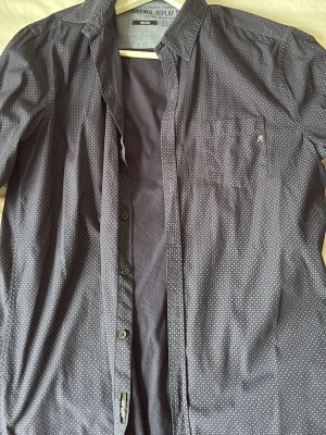 Mörkblå prickig skjorta Replay - Snygg mörkblå skjorta från Replay med små vita prickar och bröstficka med broderad logga. Klassisk krage, knäppning framtill och lång ärm. Perfekt för dig som gillar stilrena detaljer och ett modernt uttryck.