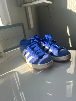 Adidas Campus blå/vita - Blå Adidas Campus  i mocka med vita klassiska stripes på sidorna och blå skosnören. Låg modell med vit sula och gummidetalj längst ner. Perfekt för dig som gillar retro och streetwear. Säljer dom då storleken tyvärr inte passade mig🩷