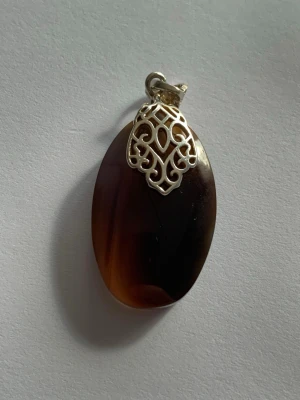 Brunt ovalt Äkta Agate sten  - Unikt halsband med en oval, brun Äkta Agate sten som har vackra färgskiftningar. Ovanpå stenen sitter en dekorativ äkta silver.  