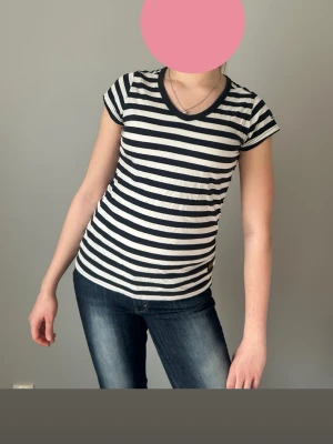 Randig svartvit t-shirt med v-ringning - Säljer en svartvit randig t-shirt med v-ringning och korta ärmar. T-shirten har en slim passform och är tillverkad i mjuk bomull, perfekt för en avslappnad och stilren look. Klassiska horisontella ränder ger en tidlös vibe.