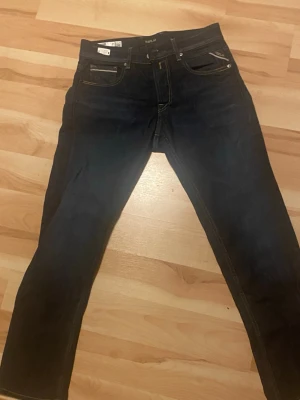 Mörkblå jeans från Replay - Snygga mörkblå jeans från Replay med klassisk femficksdesign och gulbruna kontrastsömmar. Jeansen har en smal passform och är tillverkade i ett stretchigt denimtyg för extra komfort. Perfekta för en trendig och avslappnad stil. Helt nya använda 2 gånger