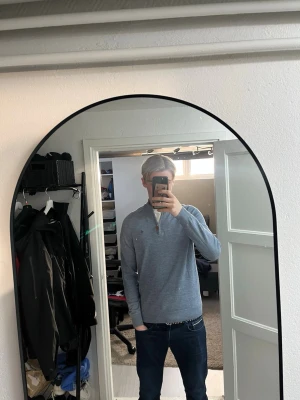 Blå stickad tröja med half zip - Snygg blå stickad tröja från Morris med halv dragkedja och brunt läderdetalj på zip. Tröjan har hög krage och en broderad logga på bröstet och är i bra skick. Jag är 178.