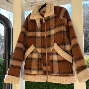 Brunrutig teddyjacka med dragkedja - Säljer en brunrutig teddyjacka med mjukt, fluffigt foder i beige. Jackan har dragkedja framtill, två snedställda fickor och bred krage. Denna är lite tjockare än de klassiska ”teddyjackorna”. 