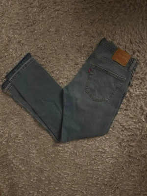 Levi's blå raka jeans - Klassiska blå Levi's jeans med rak passform och fem fickor. Jeansen har den ikoniska läderlappen bak i midjan och röd Levi's-tag på bakfickan. Tillverkade i slitstarkt denimtyg, perfekta för en avslappnad och tidlös stil.