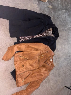 Brun biker skinnjacka med gulddragkedjor - Snygg brun skinnjacka i bikerstil med flera guldfärgade dragkedjor och detaljer. Kortare modell med markerad krage och axelparti. Perfekt för dig som vill ha en edgy look och gillar streetstyle.