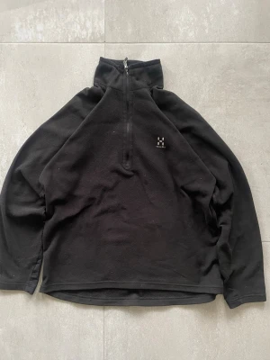 Svart fleece från Haglöfs med half zip - Mysig svart fleece från Haglöfs med hög krage och half zip framtill. Perfekt för kyliga dagar och enkel att dra på sig. Diskret Haglöfs-logga på bröstet och långärmad modell. Passar lika bra till jeans som till träningsbyxor.