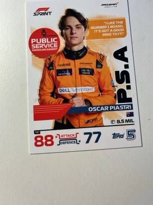 F1 samlarkort Oscar Piastri - Samlarkort från Topps med Oscar Piastri i McLaren racingdräkt. Kortet har färgstark design i orange, vitt och blått med statistik och logotyper från F1 och McLaren. Perfekt för motorsportfans och samlare.