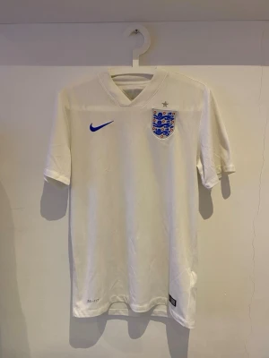 England Hemmatröja 2015 – Äkta Nike – M - Äkta England hemmatröja från 2015, tillverkad av Nike.  Storlek M. Tröjan är i fint skick utan hål eller skador. Endast en liten smutsfläck (visas på bild) som kanske kan tas bort vet inte 🤷🏻‍♂️