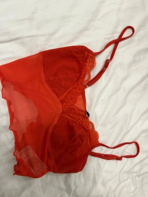 Röd spets topp med meshdetaljer - Säljer en röd topp med tunna justerbara axelband, spetskant längs bysten och meshpartier på sidorna. Toppen är nästan helt oanvänd och är perfekt för sommaren. 