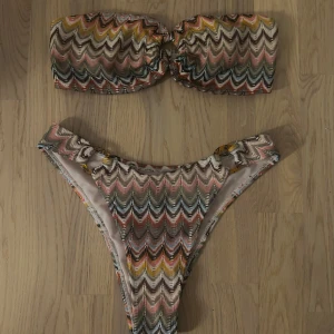 Mönstrad bikini med bandeau-topp - Säljer denna jätte fina Trendig bikini med ett färgglatt mönster då den var för liten för mig tyvärr:(  Bandeau toppen har en knutdetalj framtill och matchande underdel och den är inte använd så som ny!🤍