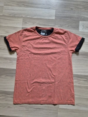 Orange t-shirt med svarta detaljer - Säljer en orange t-shirt från Groovy med svarta muddar på ärmarna. T-shirten har en klassisk passform och är tillverkad i mjuk bomull, perfekt för en avslappnad stil. Enkel och stilren design som funkar till det mesta.