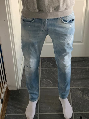 Ljusblå slitna dondup jeans med detaljer W32-W31 - Säljer ett par ljusblå dondup jeans med slitningar Jeansen har smal passform, klassiska fem fickor och coola färgstänk för en trendig look. Perfekta för dig som gillar streetstyle och vill ha något unikt i garderoben. Perfekt för sommaren nu oxå med lite ljusare färger. Den e 32 men skulle säga att den passar 31 också. Skriv vid frågor eller annat. 