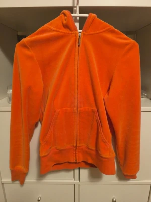 Orange Juicy Couture hoodie - Säljer en orange hoodie från Juicy Couture i mjuk velour med glittrande strassdetaljer och krona på ryggen. Hoodien har dragkedja framtill, huva och två fickor. 