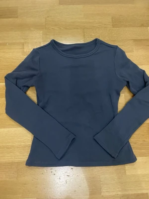 Grå långärmad topp - En enkel och stilren långärmad topp med rund halsringning. Toppen har en tight passform och är tillverkad i ett mjukt, stretchigt material som känns skönt mot huden. Perfekt att matcha med jeans eller kjol för en clean look.
