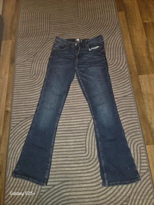 Mörkblå bootcut jeans - Snygga mörkblå bootcut jeans med klassisk femficksdesign och knappgylf. Jeansen har en lätt utsvängd passform nedtill och är tillverkade i denim. Perfekta för dig som gillar en retroinspirerad look och vill ha ett par jeans som sticker ut lite extra.