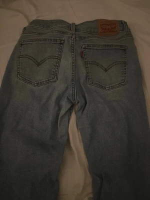 Levi's ljusblå raka jeans - Ljusblå jeans från Levi's med klassiska raka ben och femficksmodell. Jeansen har tydliga sömmar på bakfickorna och en brun läderpatch med Levi's-logga bak i midjan. Tillverkade i slitstark denim, perfekt för en avslappnad look.