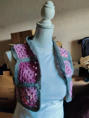 Virkad väst i rosa och lila toner - Rosa/grå väst  35cm över axlarna  36cm lång  Akrylgarn