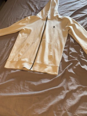 Beige hoodie från Polo Ralph Lauren - Snygg beige hoodie med dragkedja från Polo Ralph Lauren. Klassisk design med huva, två fickor framtill och den ikoniska mörkblå loggan broderad på bröstet. Tillverkad i mjukt bomullsmaterial som är skönt att ha på sig. Perfekt för en avslappnad och stilren look. priset kan diskuteras!