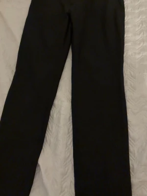 Svarta raka herr kostymbyxor - Säljer ett par klassiska svarta kostymbyxor med rak passform. Byxorna har diskreta bakfickor och är sydda i ett slätt tyg som ger en stilren look. Perfekta för dig som vill ha en clean och enkel stil.