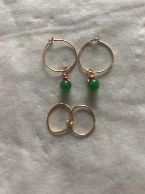 Guldörhängen 18K hoops med gröna jade hängen - Säljer två par örhängen i tunn äkta guld... Ett par är hoops med små gröna pärlor jade Sten, det andra paret är enkla guldfärgade hoops utan hänge som det går att flyttas. Ena paret ca 1cm i diameter den andra mindre ca 0,5cm i diameter. Passar små barn då är de fjäderlätta. Perfekta för dig som gillar minimalistisk stil. 800kr paret.