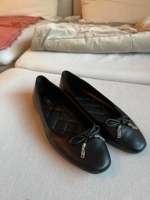 Michael Kors  ballerinaskor  - Använda två gånger!Säljer ett par svarta ballerinaskor i läder med quiltad innersula. Skorna har rundad tå och dekorativa rosetter framtill med silverfärgade kedjor som detalj. Perfekta för dig som gillar en stilren och trendig look.