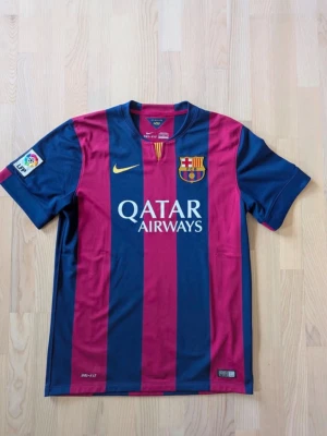Barcelona matchtröja Nike blå/röd - Säljer en FC Barcelona matchtröja från Nike med breda blå och röda ränder. Tröjan har klubbmärke, Qatar Airways-tryck på bröstet och UNICEF-logga på ryggen. Korta ärmar och officiell La Liga-patch på ärmen. Perfekt för fotbollsfans!