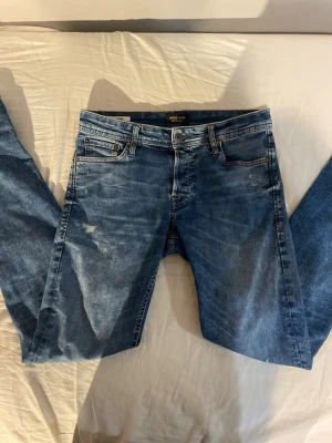 Blå jeans från Jack & Jones - Säljer nu dessa slim jeans från Jack Jones med fina slitningar. Storleken är 30/34 men sitter som 30/32. Inga defekter