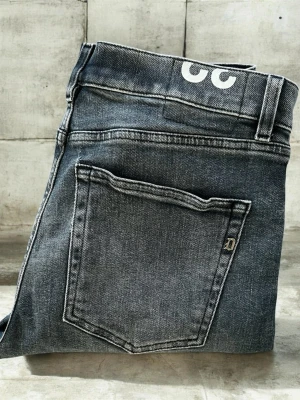 Grå jeans från dondup  - Säljer ett par grå jeans från dondup med raka ben och klassiska bakfickor. Jeansen har en cool vintage-wash och detaljer som D-logga på fickan. Perfekt för dig som gillar en avslappnad och stilren look. Modelen är icon