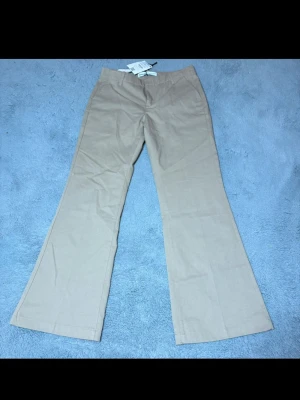 Beiga utsvängda kostymbyxor - Snygga beiga kostymbyxor med utsvängda ben och hög midja. Byxorna har klassisk design med hällor för skärp och diskreta fickor. Perfekta för en stilren look. 