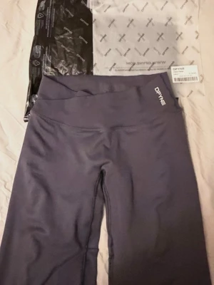 DFYNE vision flares regular  - Mörkgrå träningstights från DFYNE med hög midja och bred linning. Tightsen har en stilren design med logga på både fram- och baksidan. Tillverkade i ett stretchigt och mjukt material som passar perfekt för gym, yoga eller löpning.