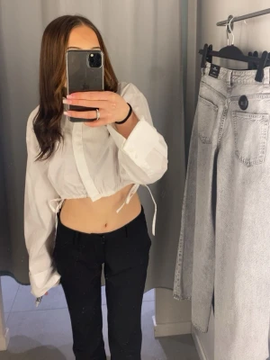 Vit croppad skjorta  - Trendig vit croppad blus med långa ärmar och snörning i midjan. Blusen har en avslappnad passform och är perfekt för att styla med både jeans och kostymbyxor. Aldrig använd 